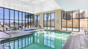 Une piscine intérieure avec des parois en verre transparent, des chaises longues et une vue sur l’extérieur.