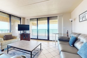A modern living room with a sofa, a coffee table, a TV, and a balcony with a view. - Luxury Perks, Corner 3br: Suntide III - Unit 1001 (South Padre Island)