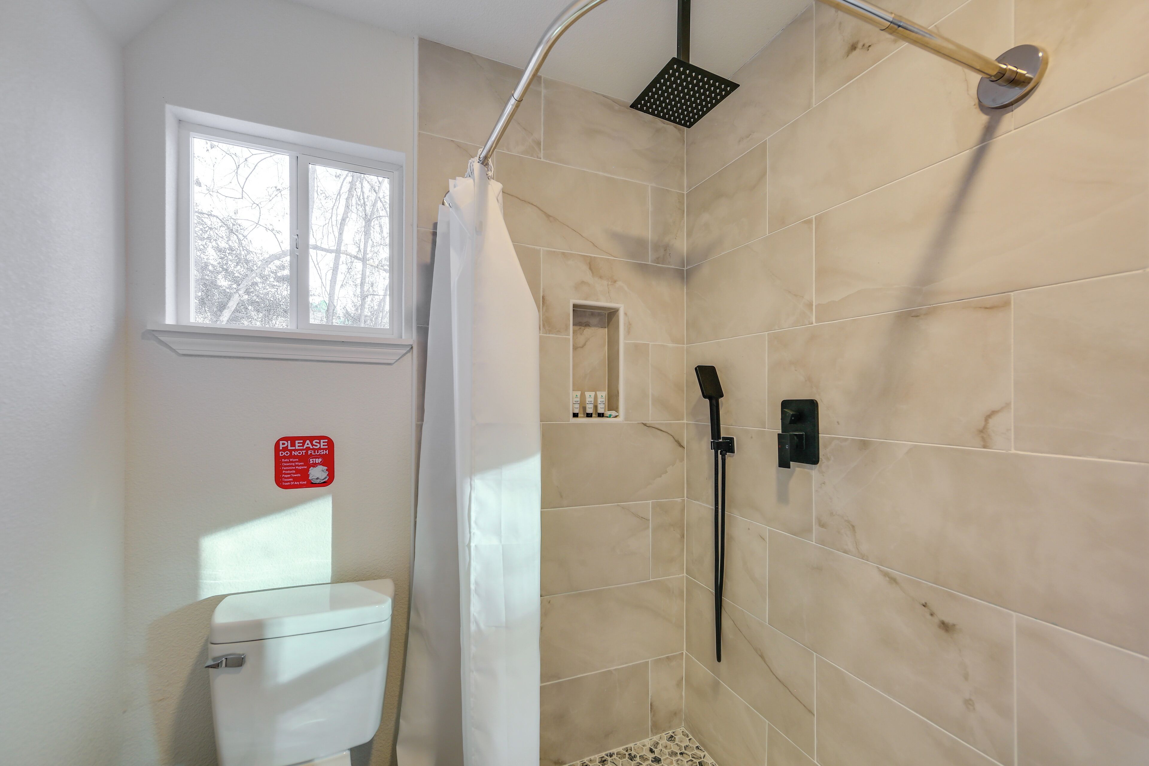 Ein Badezimmer mit Dusche, Toilette und einem Fenster.