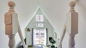Ein Zimmer mit hohen Decken, einem geneigten Dach, einem großen Fenster und Blick ins Freie.