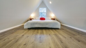 A bedroom with a sloped ceiling, a large window, a bed with white bedding and a red pillow, and two bedside lamps. - Romantic A-frame Retreat w/ Fire Pit + Hammocks (Hawkins)