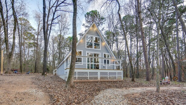 A cabin with a triangular roof, surrounded by trees, with a deck and a gravel path leading to it. - Romantic A-frame Retreat w/ Fire Pit + Hammocks (Hawkins)