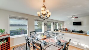 A dining area with a large table set for six, a chandelier, and a view of the outdoors. - Private Beach, Deck & Grill! Siuslaw River Getaway (Florence)