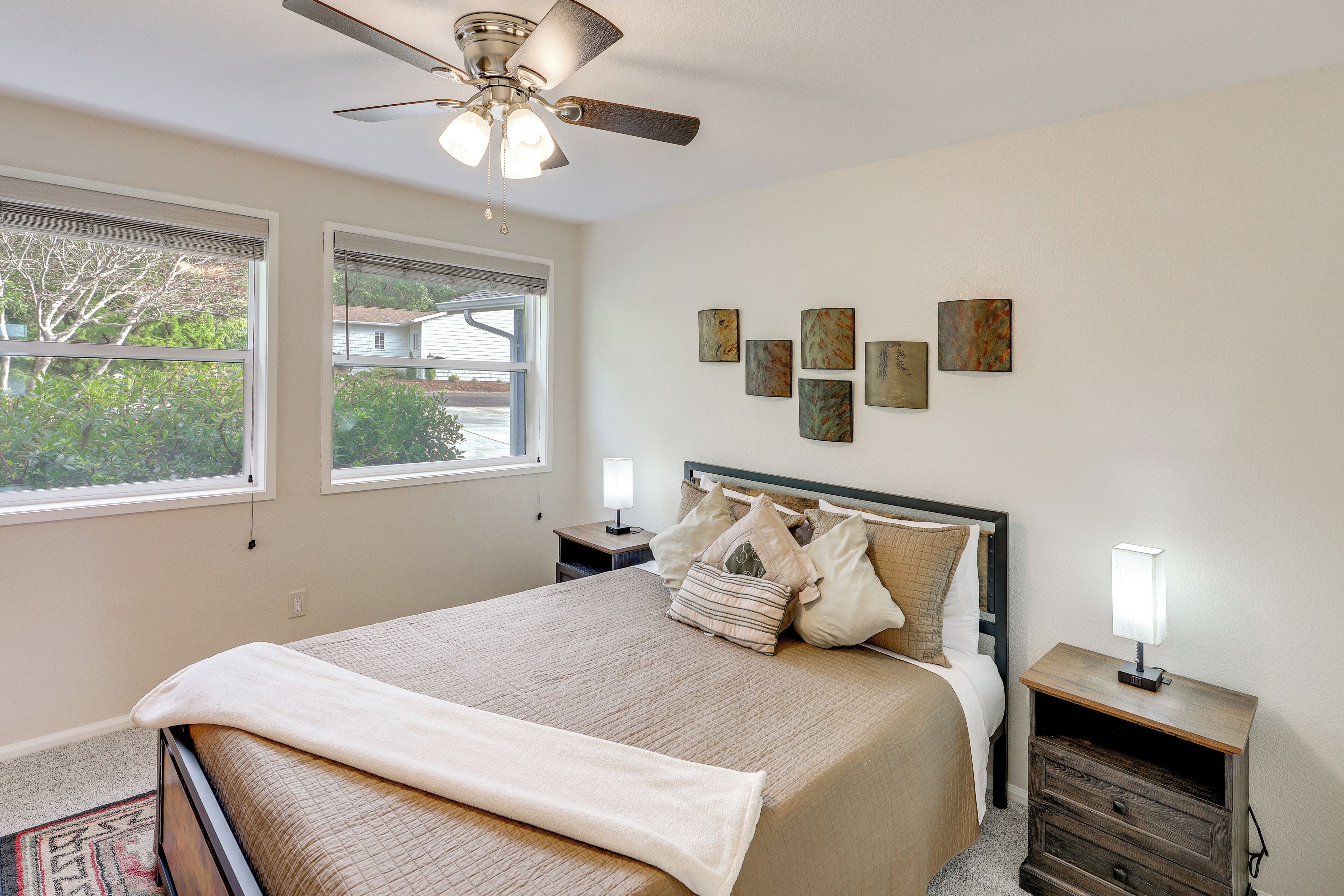 A bedroom with a bed, a nightstand, a ceiling fan, and artwork on the wall.