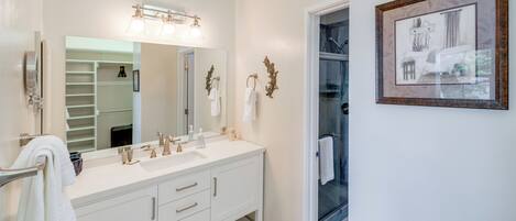 A modern bathroom with a double vanity, a large mirror, and a framed picture on the wall.