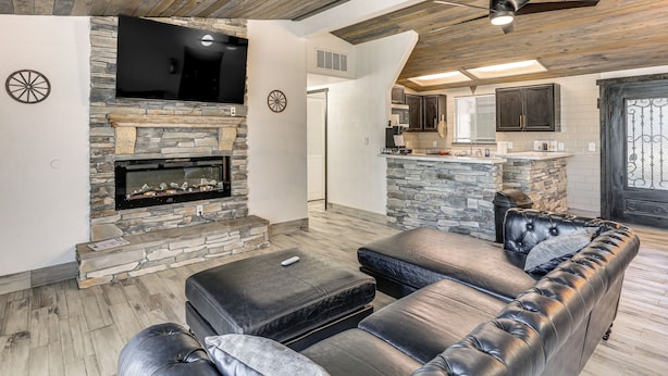 A modern living room with a stone fireplace, leather sofa, and a flat-screen TV mounted on the wall. - 1 Mi to Main St Eats! Single-level Red Bluff Home (Red Bluff)