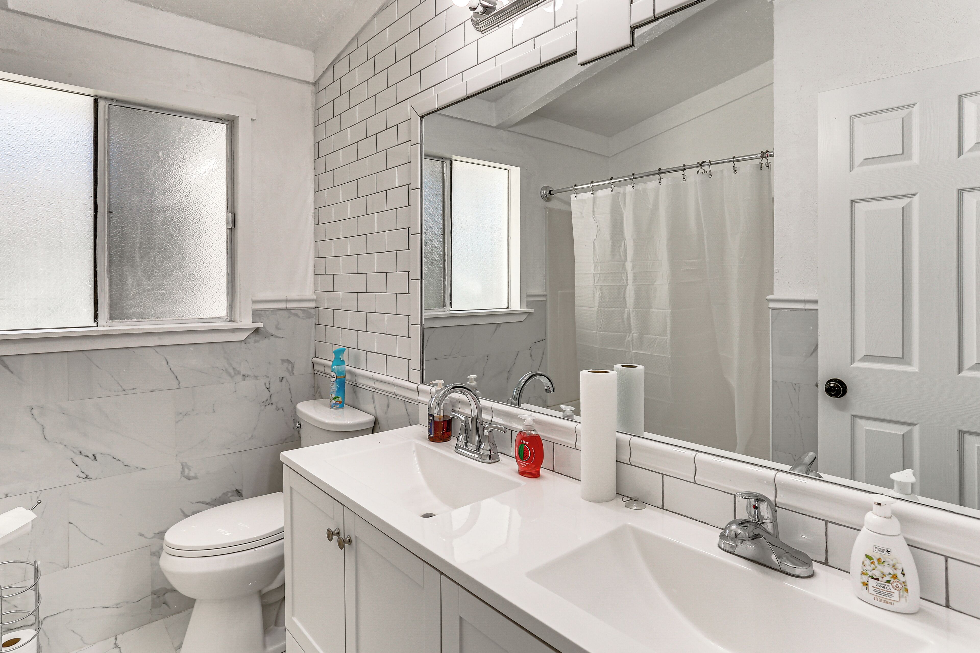 Une salle de bain avec des toilettes blanches, un lavabo avec un miroir et un rideau de douche.
