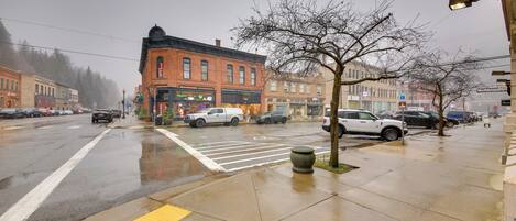 A wet street with cars parked along the sidewalk, a crosswalk, and a building with a brick facade.