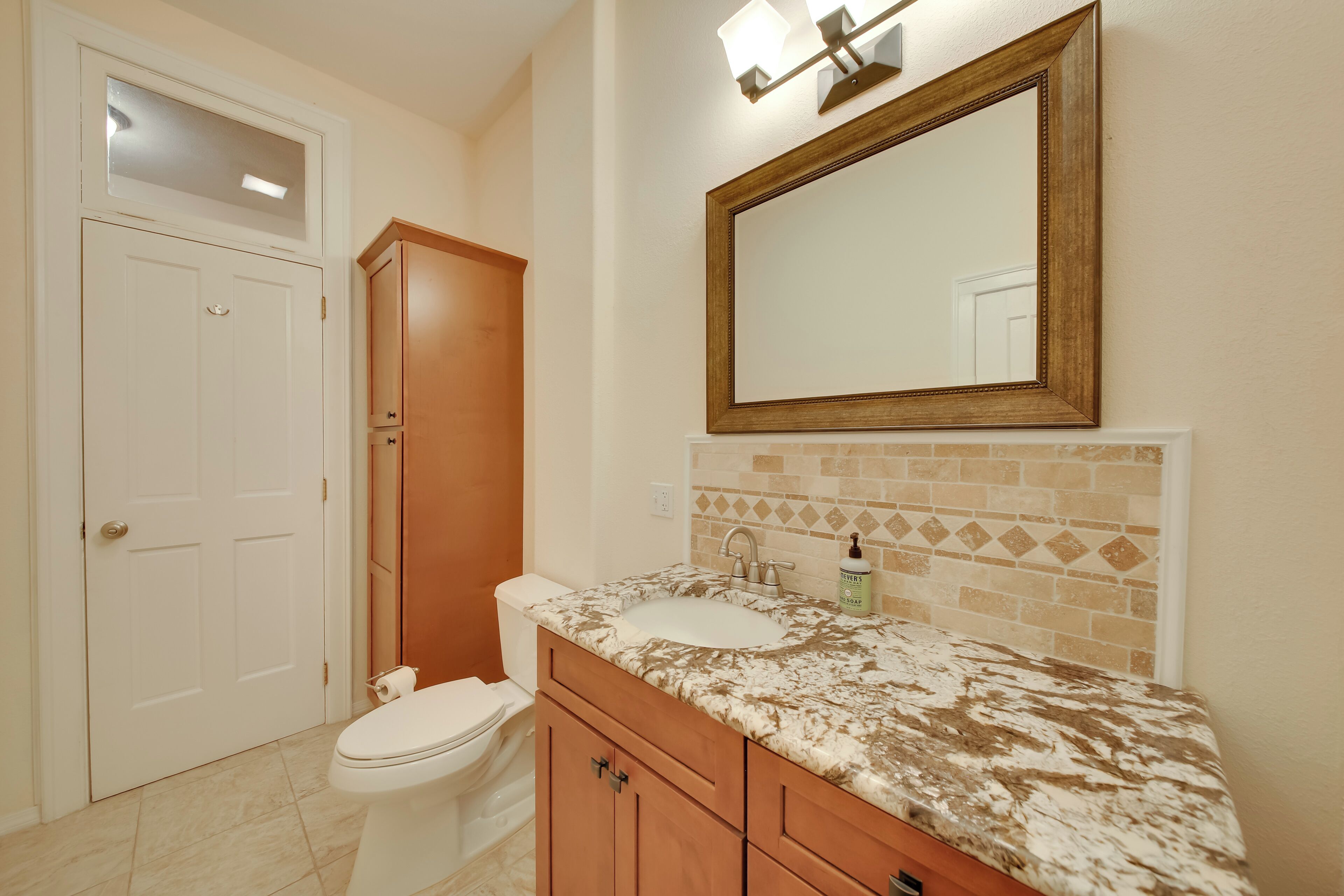 A bathroom with a toilet, vanity with a sink, and a large mirror.