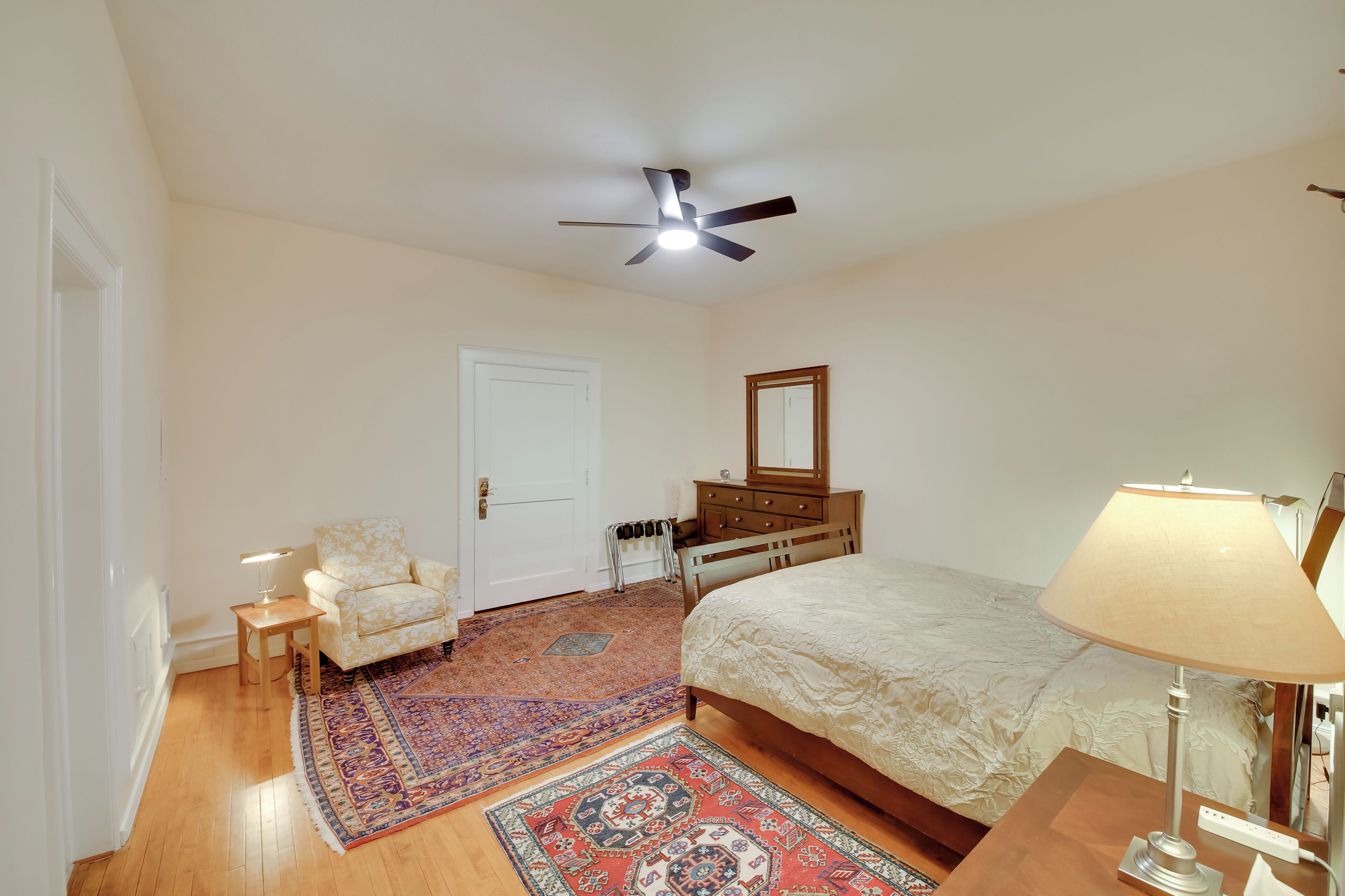 A bedroom with a bed, a nightstand, a chair, a dresser, a mirror, a ceiling fan, and a rug.