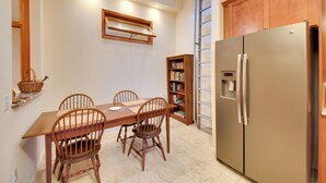 Un comedor con una mesa y sillas de madera, una estantería, un refrigerador y un tragaluz.