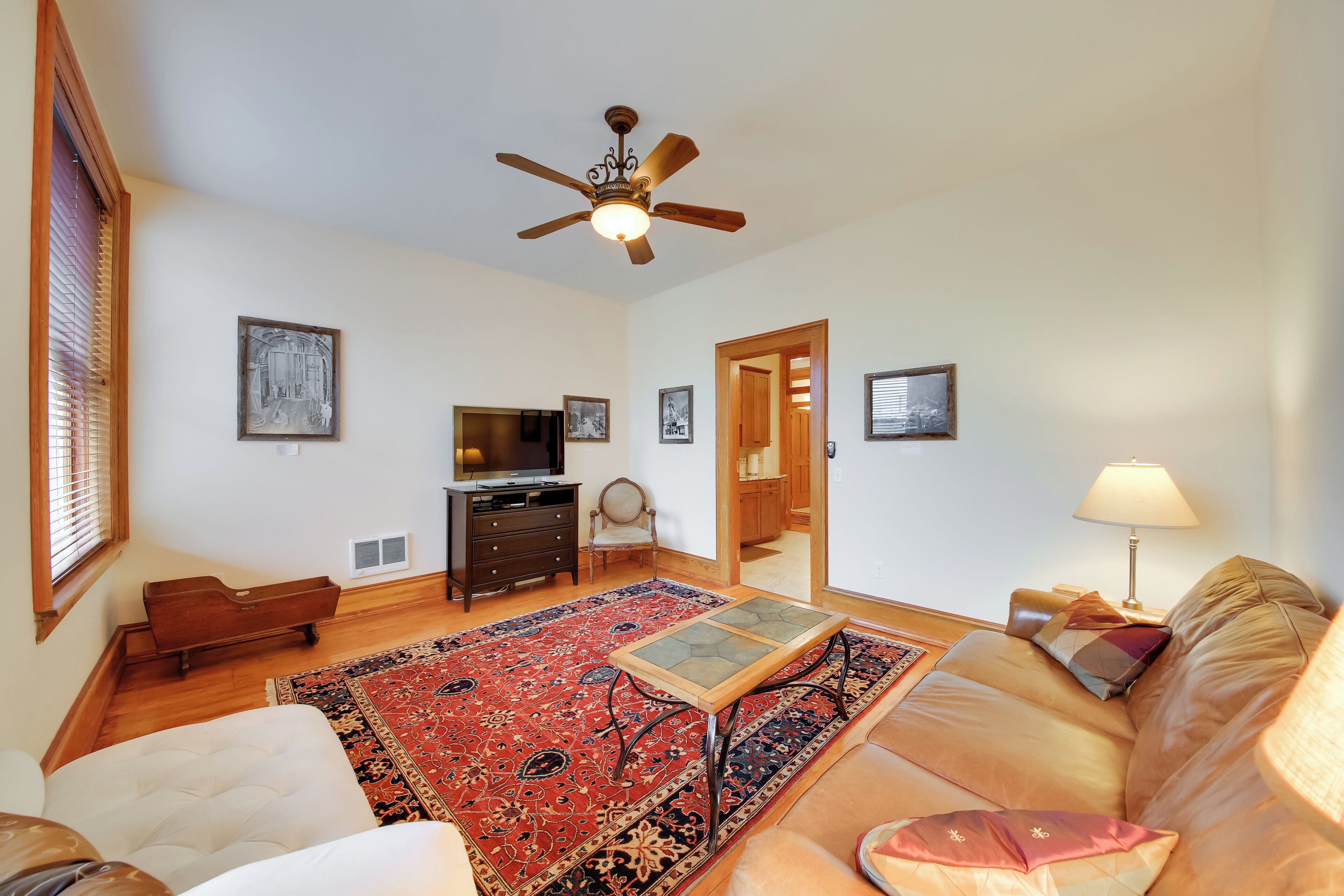 A living room with a sofa, a coffee table, a television, a ceiling fan, and a red patterned rug.