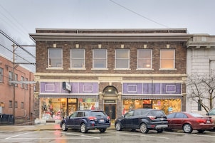 A two-story building with a brick facade, multiple storefronts, and parked cars in front.