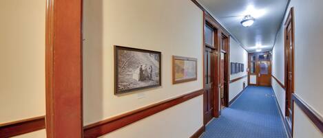 A hotel hallway with framed pictures on the walls, wooden trim, and a blue carpet.