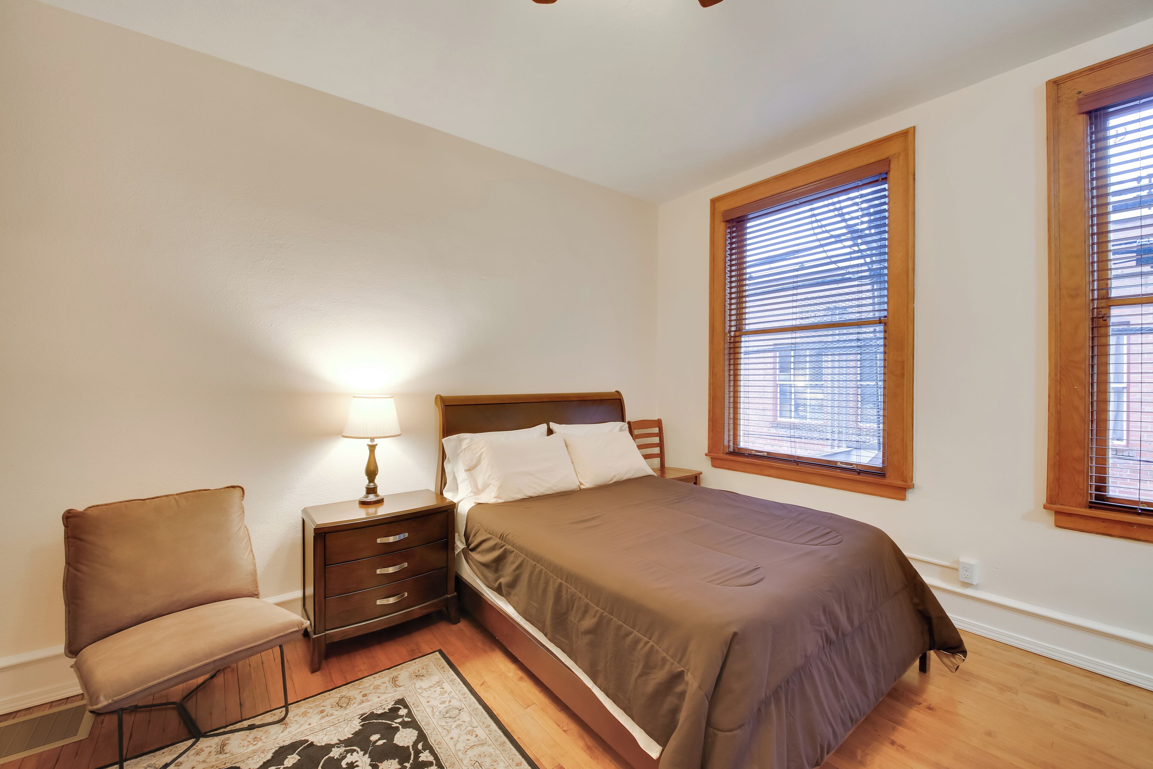 A bedroom with a bed, nightstand, chair, and a window with blinds.