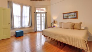 A bedroom with a bed, a window with curtains, a door, and a small blue suitcase. - Historic Allman Brothers House in Downtown Macon! (Macon)