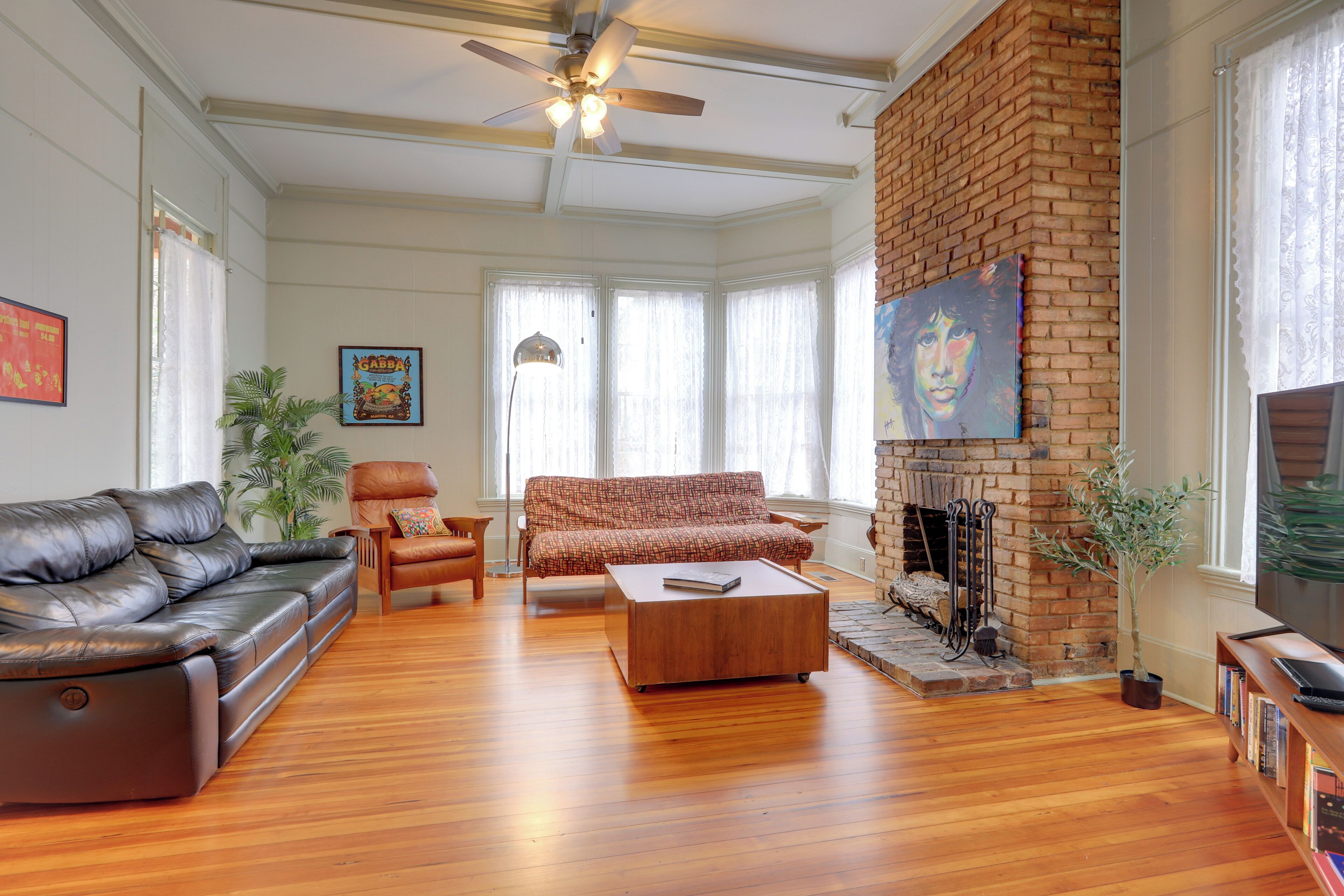 A spacious living room with a leather sofa, a wooden coffee table, a brick fireplace, and a television on a wooden stand.