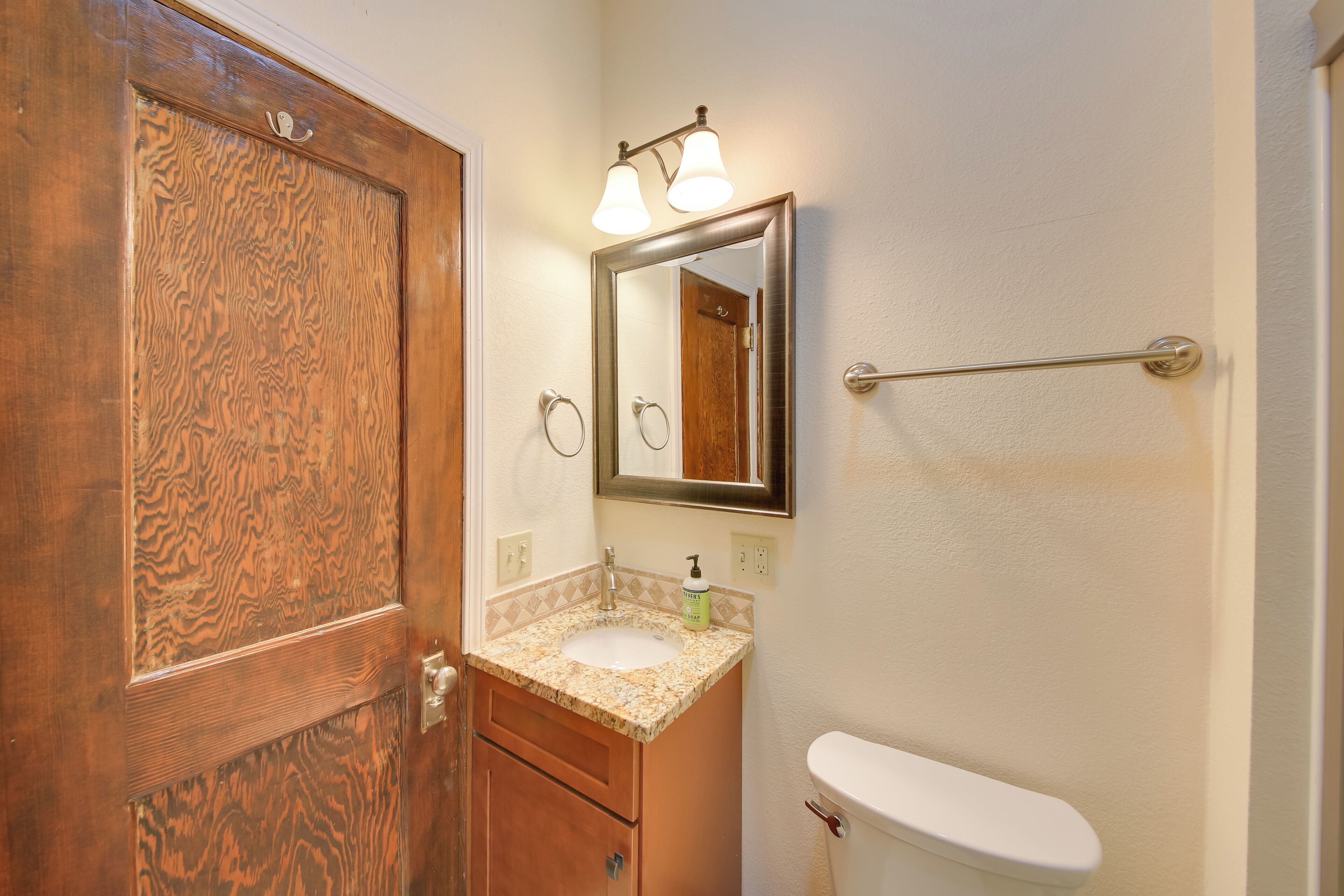 Un baño con puerta de madera, un lavabo con espejo y un inodoro.