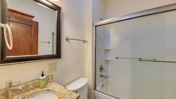 Un baño con lavamanos de encimera de granito, espejo, inodoro y ducha con mampara de vidrio.