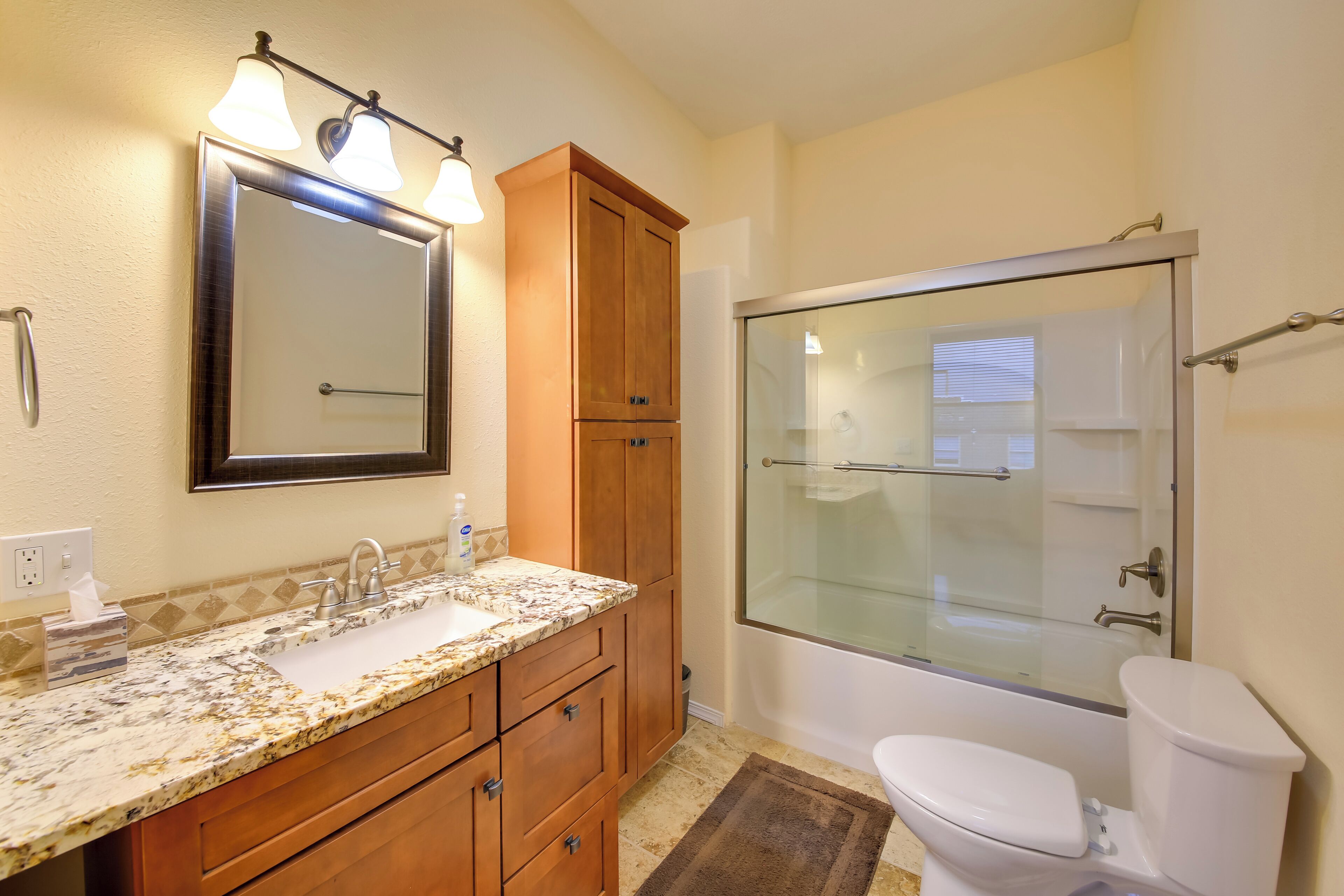A bathroom with a marble sink, wooden cabinets, a glass shower enclosure, and a white toilet.