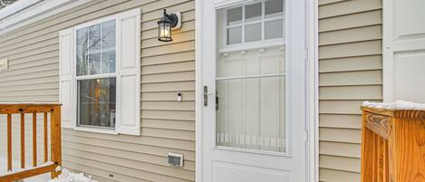 A house with a white front door, a window, and a porch with a wooden railing.