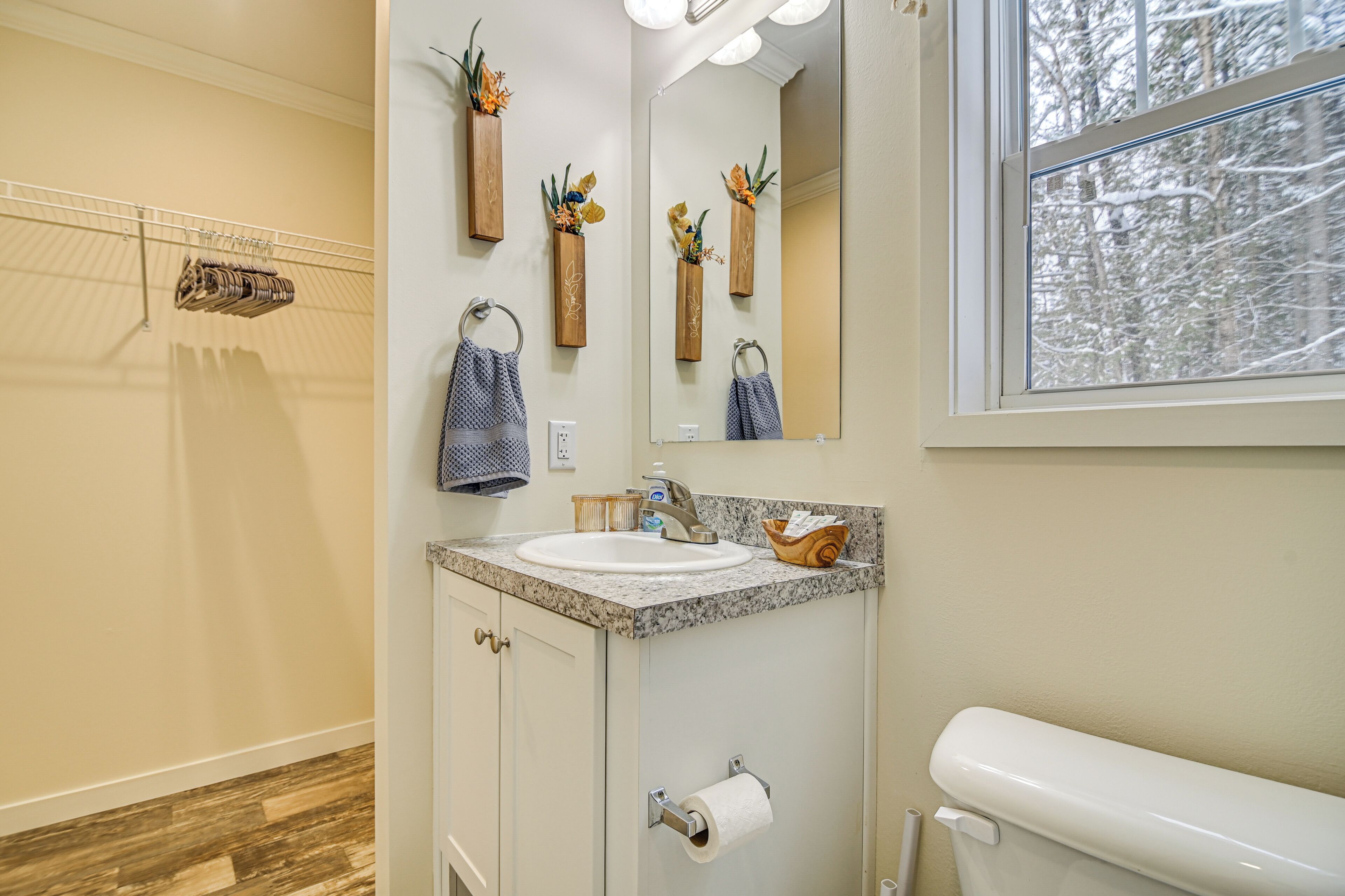 A bathroom with a sink, mirror, toilet, and a window with a view of trees.