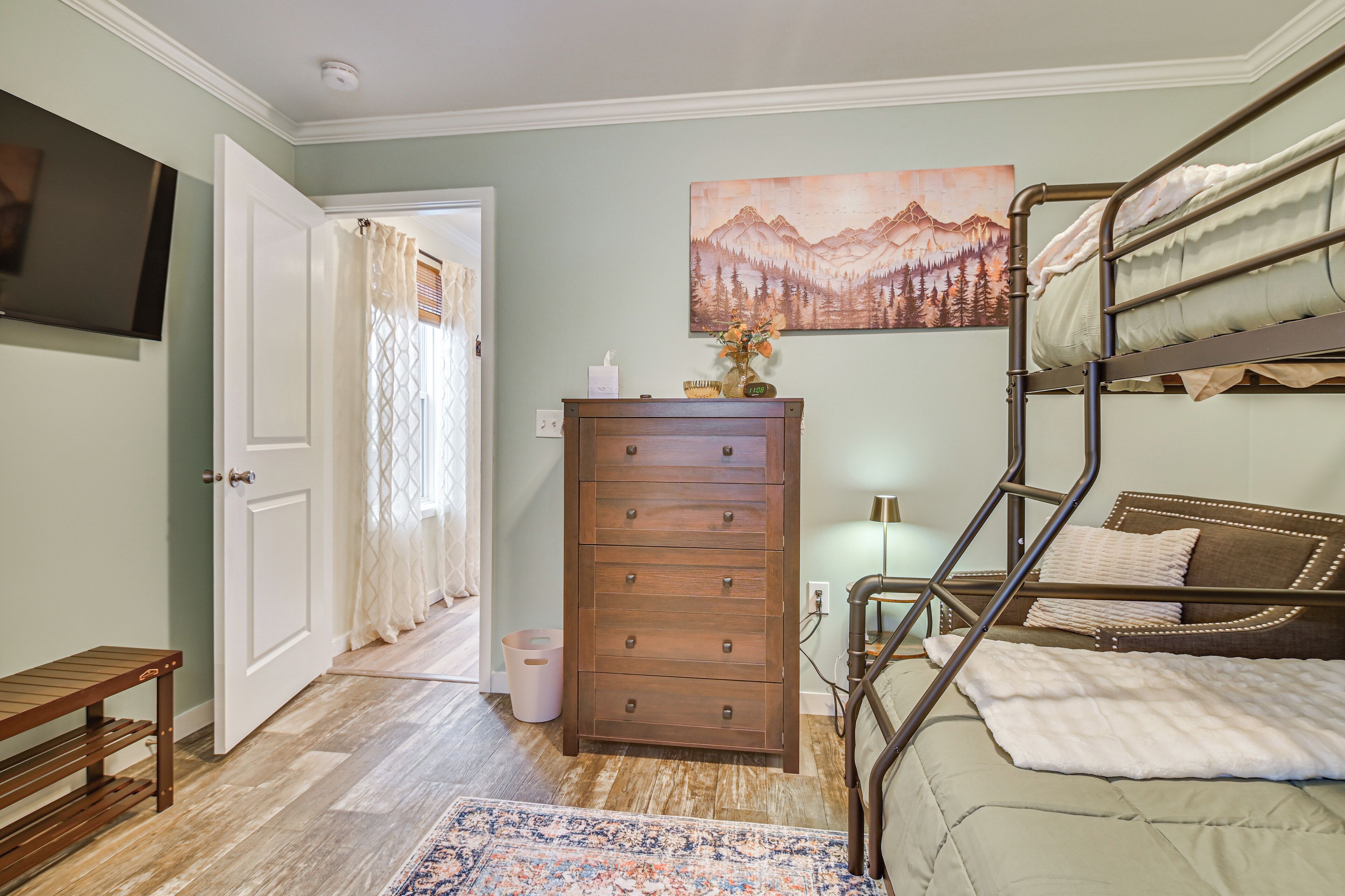 A bedroom with bunk beds, a dresser, a TV, and a painting on the wall.