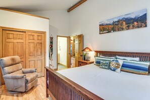 A bedroom with a wooden bed frame, a reclining chair, and a large window with a mountain view. - Scenic Creekside Retreat! Rocky Mountain Cabin (Dumont)