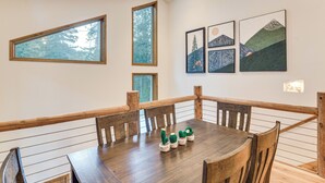 A dining area with a wooden table and chairs, framed artwork on the wall, and large windows. - Scenic Creekside Retreat! Rocky Mountain Cabin (Dumont)
