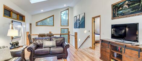 A spacious living room with a leather sofa, wooden coffee table, and a TV on a wooden stand.