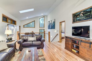 A spacious living room with a leather sofa, wooden coffee table, and a TV on a wooden stand. - Scenic Creekside Retreat! Rocky Mountain Cabin (Dumont)