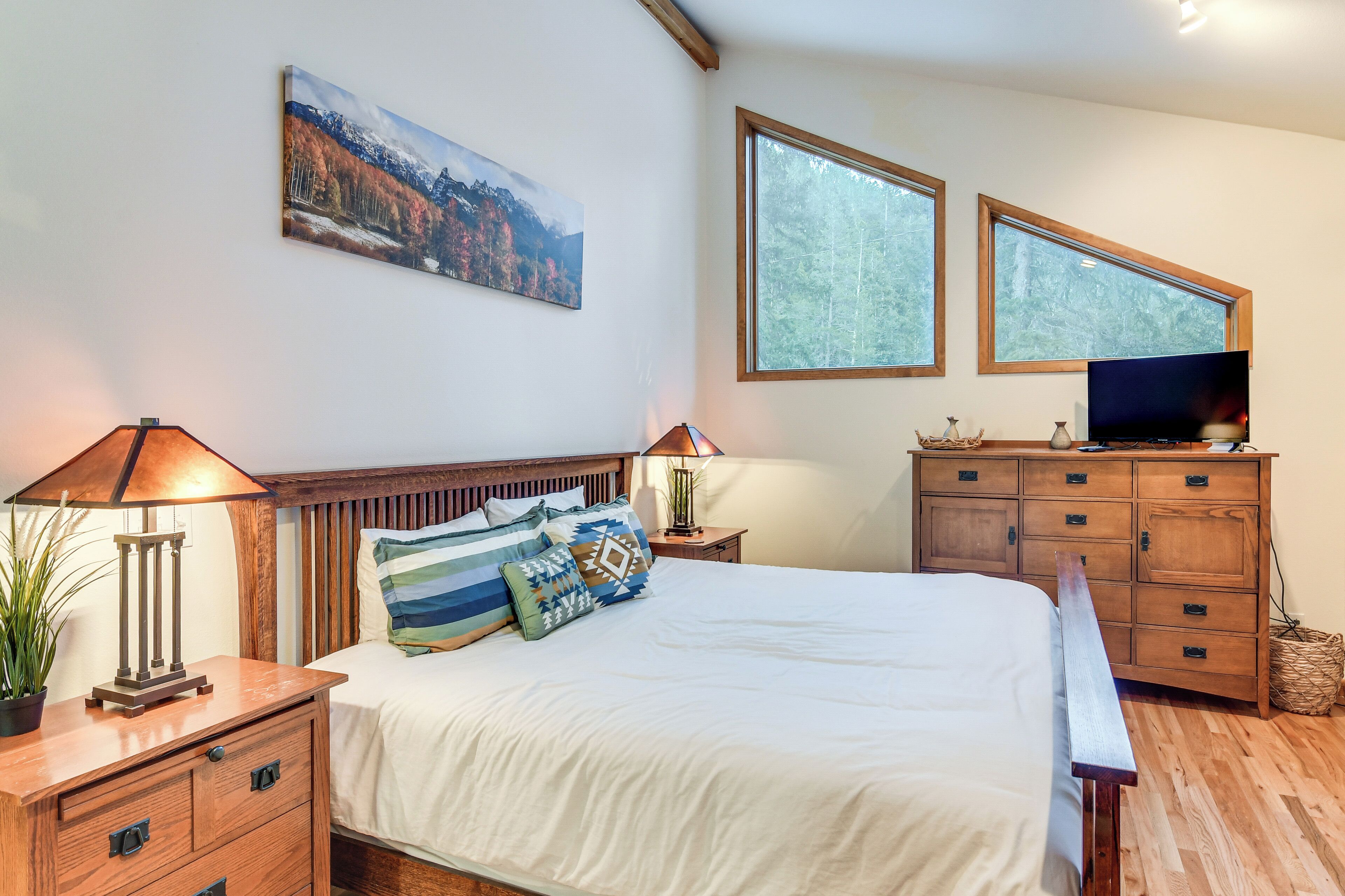 A bedroom with a bed, wooden headboard, two bedside tables with lamps, a dresser, and a television.