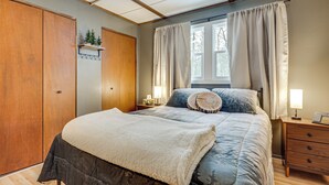 A bedroom with a large bed, wooden wardrobe, and a window with curtains. - George Lake Views & Access! Family Condo By Trails (Rhinelander)