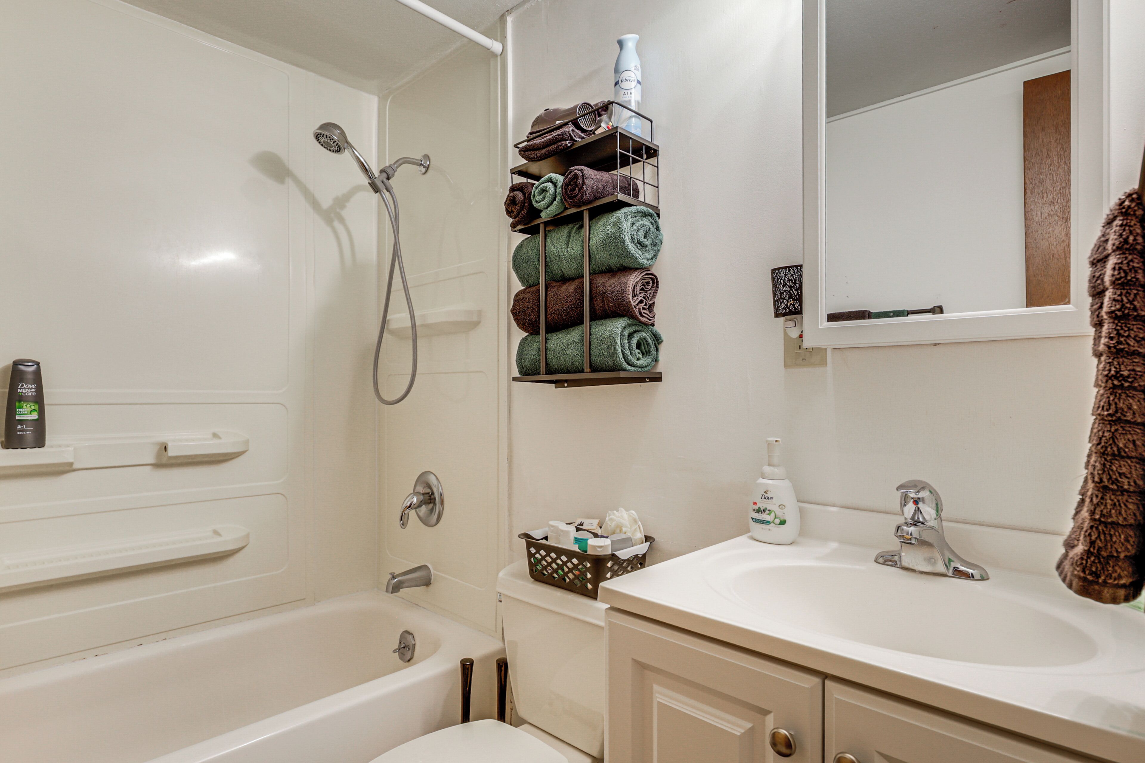 A bathroom with a bathtub, a sink, a mirror, and a towel rack with folded towels.