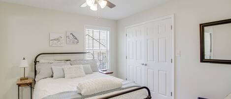 A bedroom with a bed, a ceiling fan, a window with blinds, a door, and a mirror on the wall.