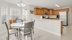 A modern kitchen with wooden cabinets, a white island, and a dining area with chairs. - 2 Mi to Pickwick Landing State Park: Home w/ Yard (Counce)