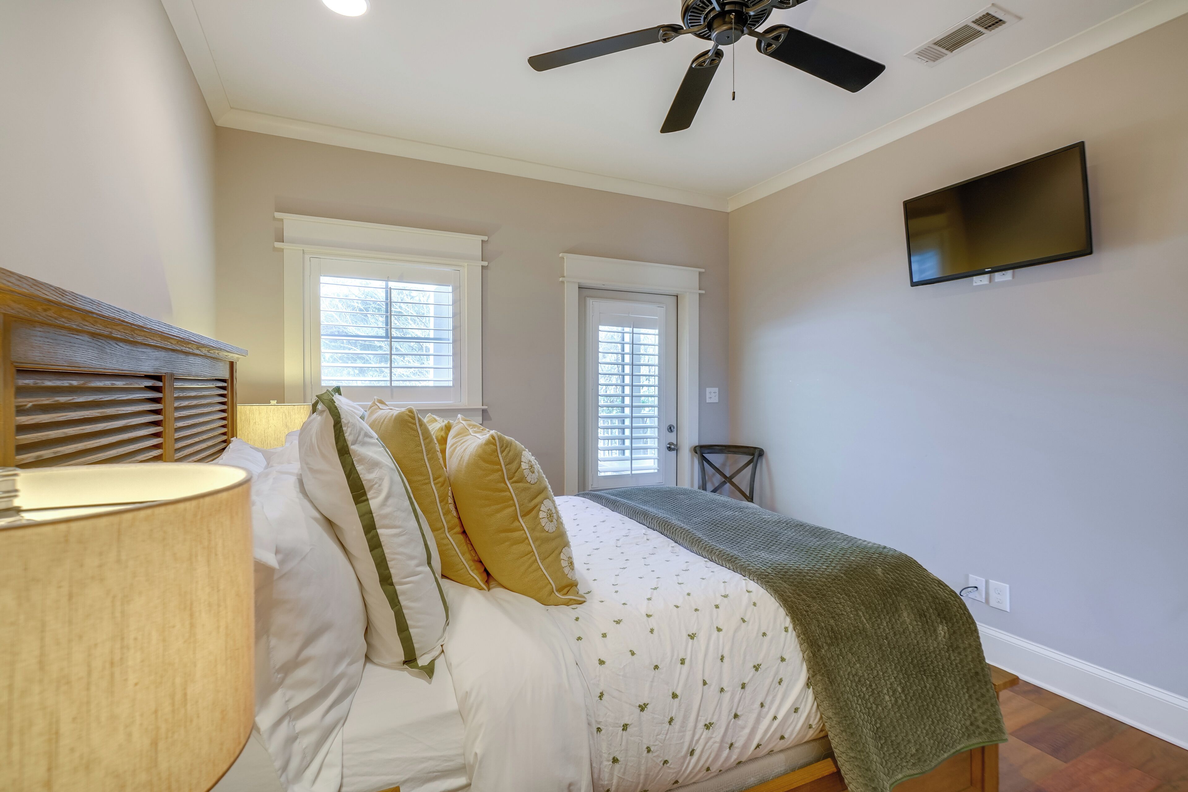 A bedroom with a bed, a ceiling fan, a TV, and two windows.