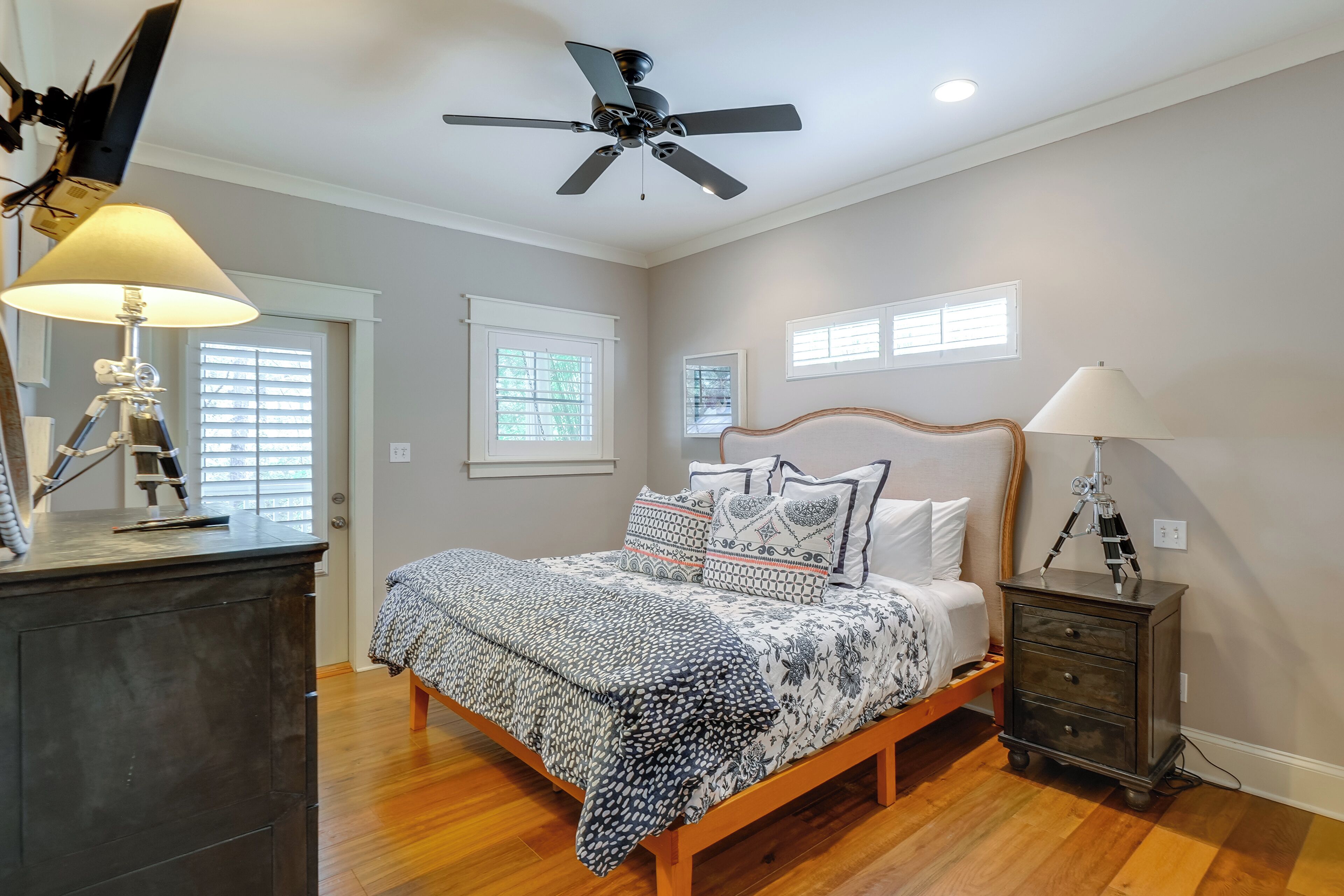 A bedroom with a bed, a desk, a lamp, a ceiling fan, and a nightstand.