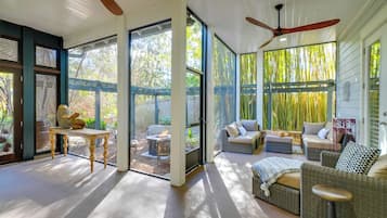 Une vaste terrasse dotée de meubles en osier, de grandes portes-fenêtres coulissantes et d’un ventilateur de plafond.