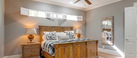 Un dormitorio con una cama de madera, dos mesitas de noche, un ventilador de techo y un espejo grande.