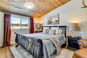 Un dormitorio con cama, techo de madera, ventana con cortinas y un cuadro en la pared.