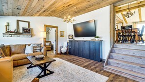 A spacious living room with a wooden ceiling, a large flat-screen TV, a dining area with a chandelier, and a staircase leading to another level. - 'luna Ranchhouse' Nestled Among the Pines! (Luna)