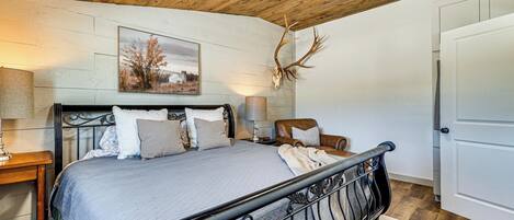 Une chambre à coucher avec un lit, une chaise, une lampe et un crâne de cerf accroché au mur.