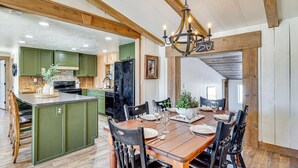 A spacious kitchen with green cabinets, a wooden dining table set for six, and a chandelier. - 'luna Ranchhouse' Nestled Among the Pines! (Luna)