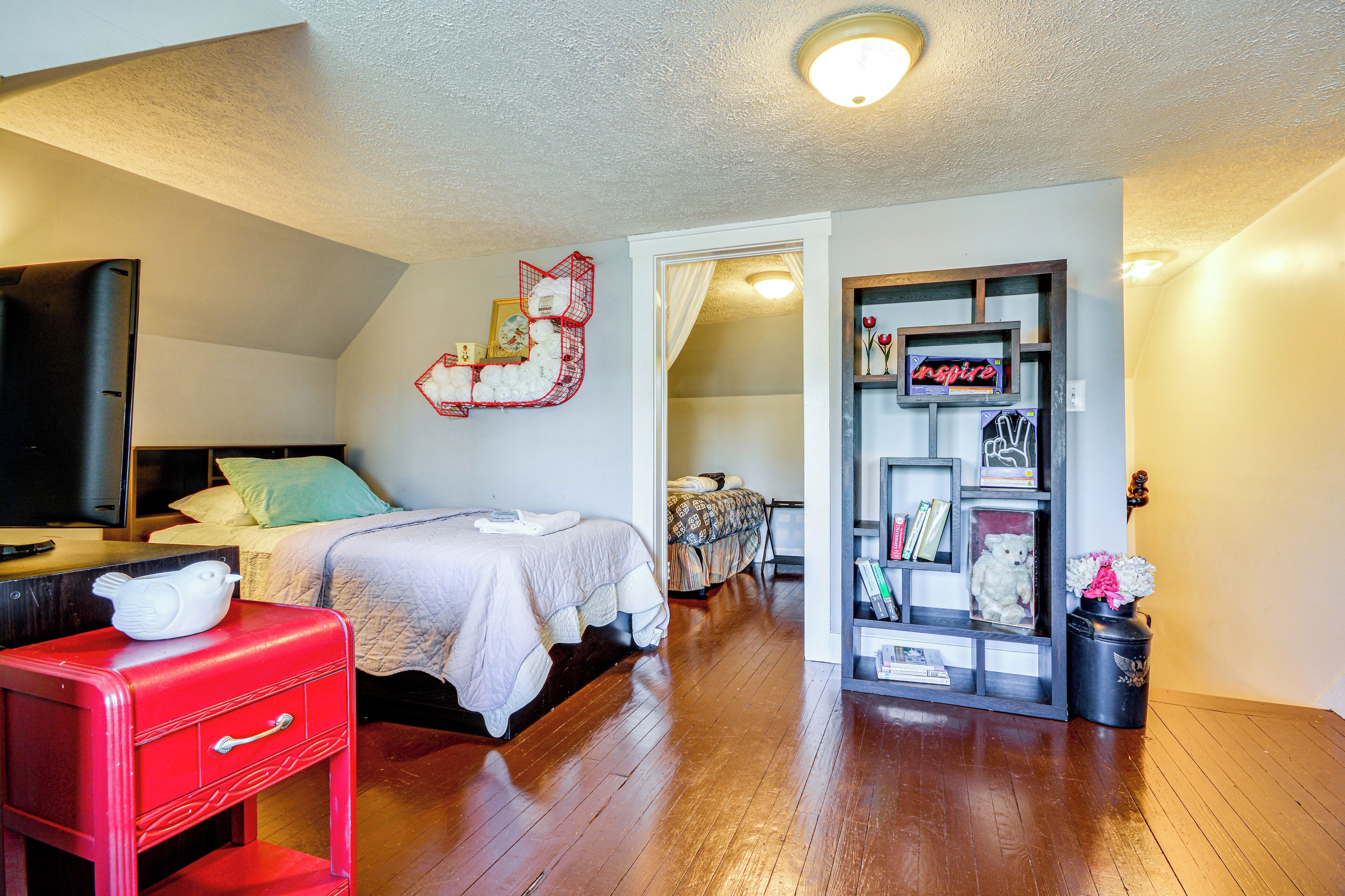 Une chambre à coucher avec un lit, une commode rouge, une bibliothèque et une porte donnant sur une autre pièce.