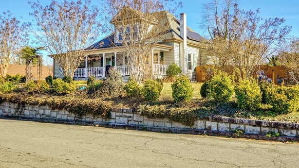 A two-story house with a porch, surrounded by mature trees and a stone wall. - 'storybook Craftsman' Home w/ Private Hot Tub! (Mount Airy)