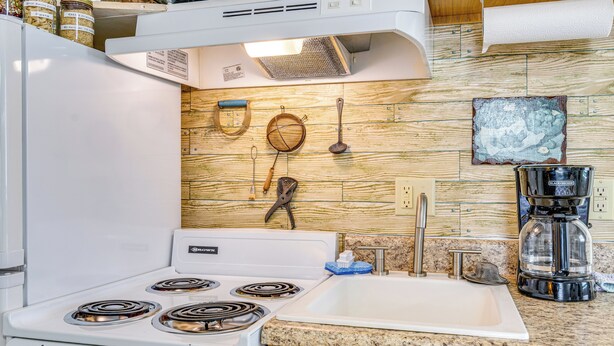 Una cucina con un piano cottura bianco, un ripiano in granito, un lavello e diversi utensili da cucina appesi al muro.