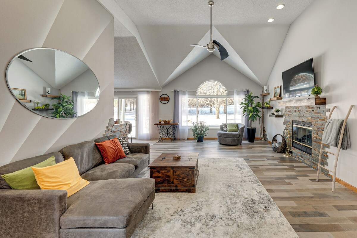 A spacious living room with a large mirror, a grey sofa with colorful cushions, a wooden coffee table, and a fireplace with a brick surround.