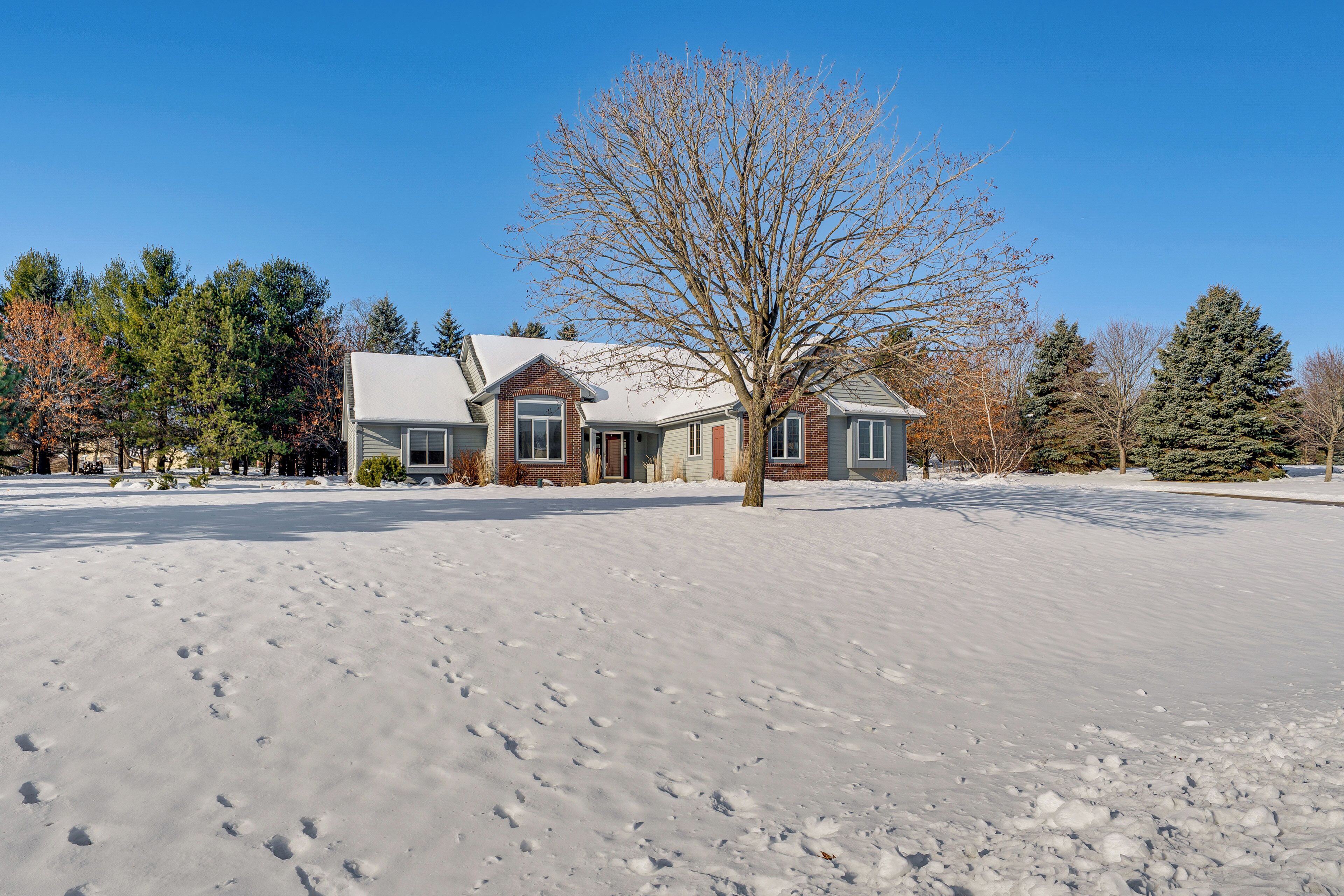 A two-story house with a snow-covered yard and a leafless tree in front.