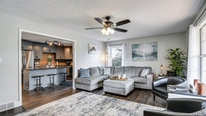 A modern living room with a grey sectional sofa, a black leather chair, and a kitchen area with a bar stool.